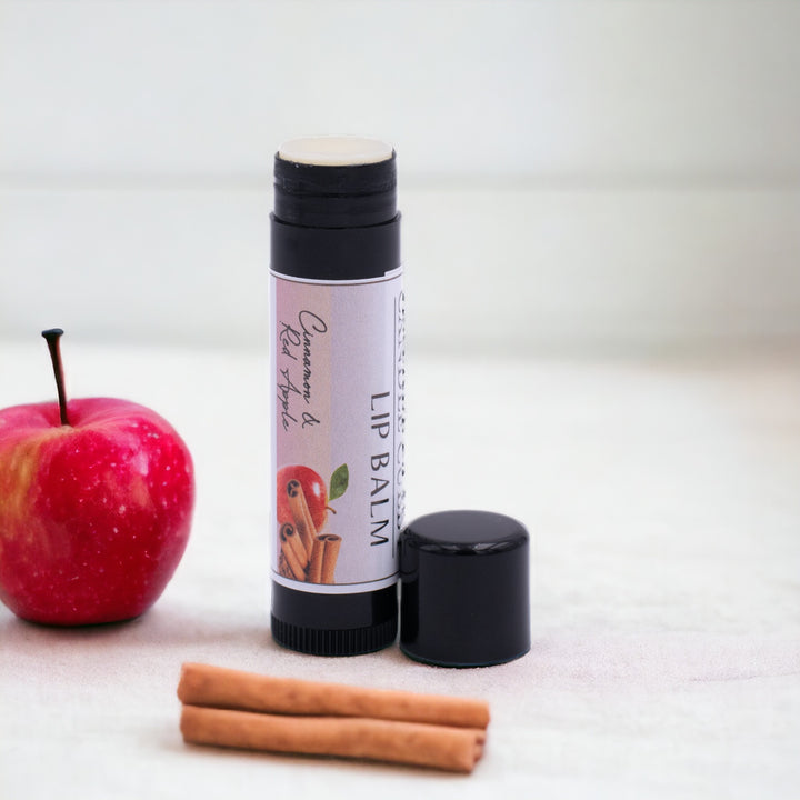 Cinnamon & Red Apple Lip Balm, Classic Tube, Cinnamon and Red Apple Flavored, Candle Cubby, Plain White Background, Countertop Photo with Apples and Cinnamon